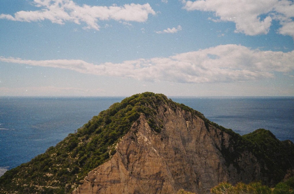 Steep rocky cliff with green vegetation overlooking the deep blue sea in Zakynthos, Greece - Landscape photography by Rocco Goldschmidt