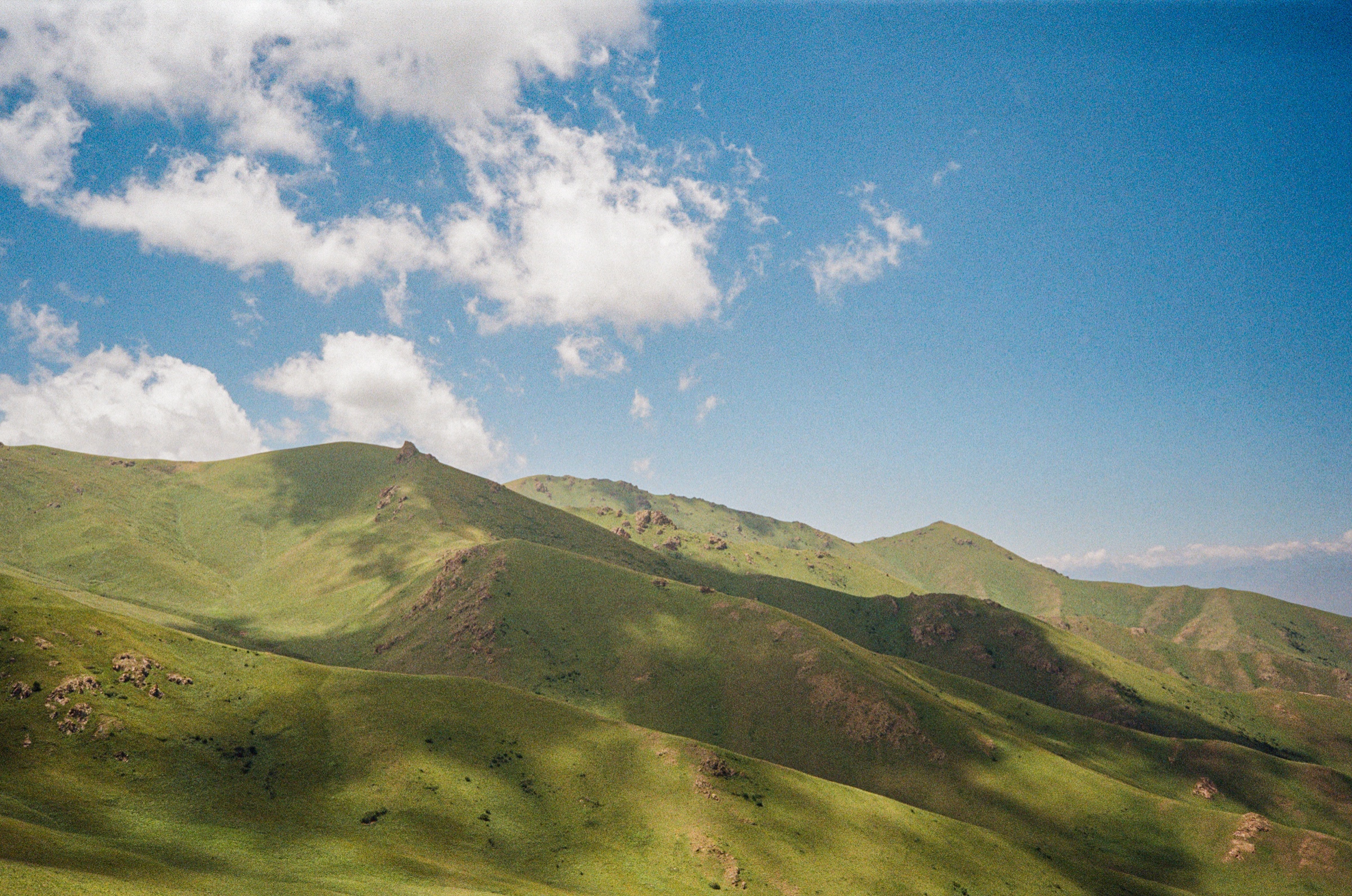 Rolling green hills under clouds in the highlands near Song-Köl, Kyrgyzstan - Landscape photography by Rocco Goldschmidt