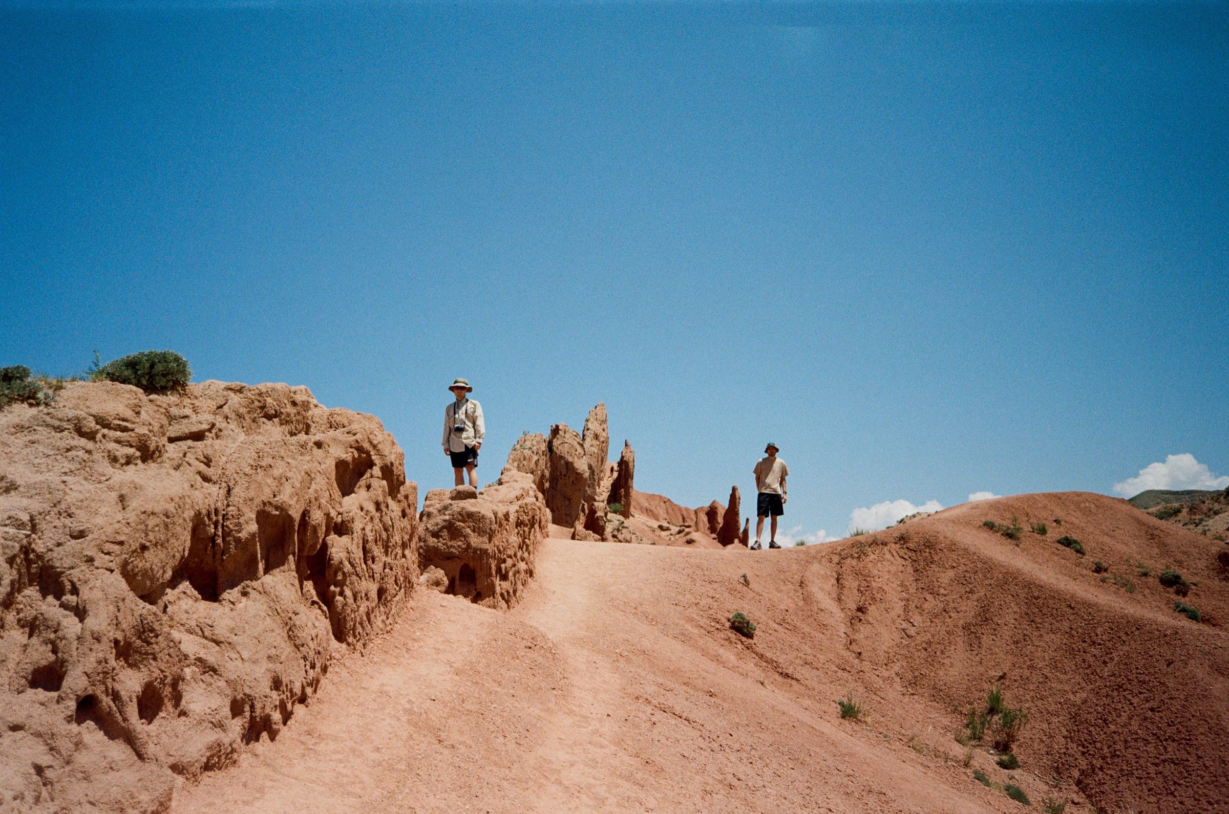 Two hikers standing on eroded red rock formations in Skazka Canyon, Kyrgyzstan - Landscape photography by Rocco Goldschmidt