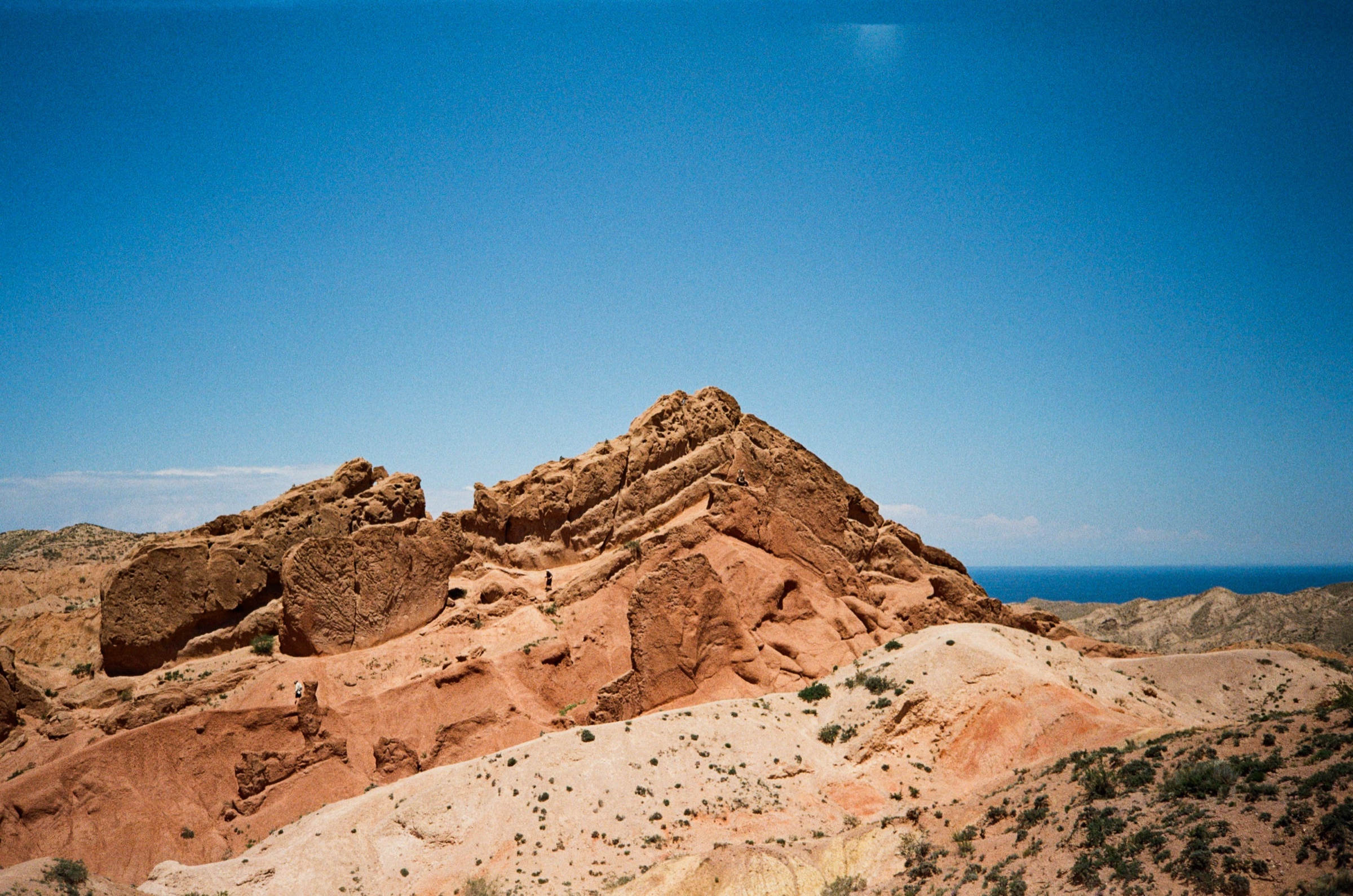 Red sandstone Skazka Canyon rock formations with Lake Issyk-Kul in the distance, Kyrgyzstan - Landscape photography by Rocco Goldschmidt