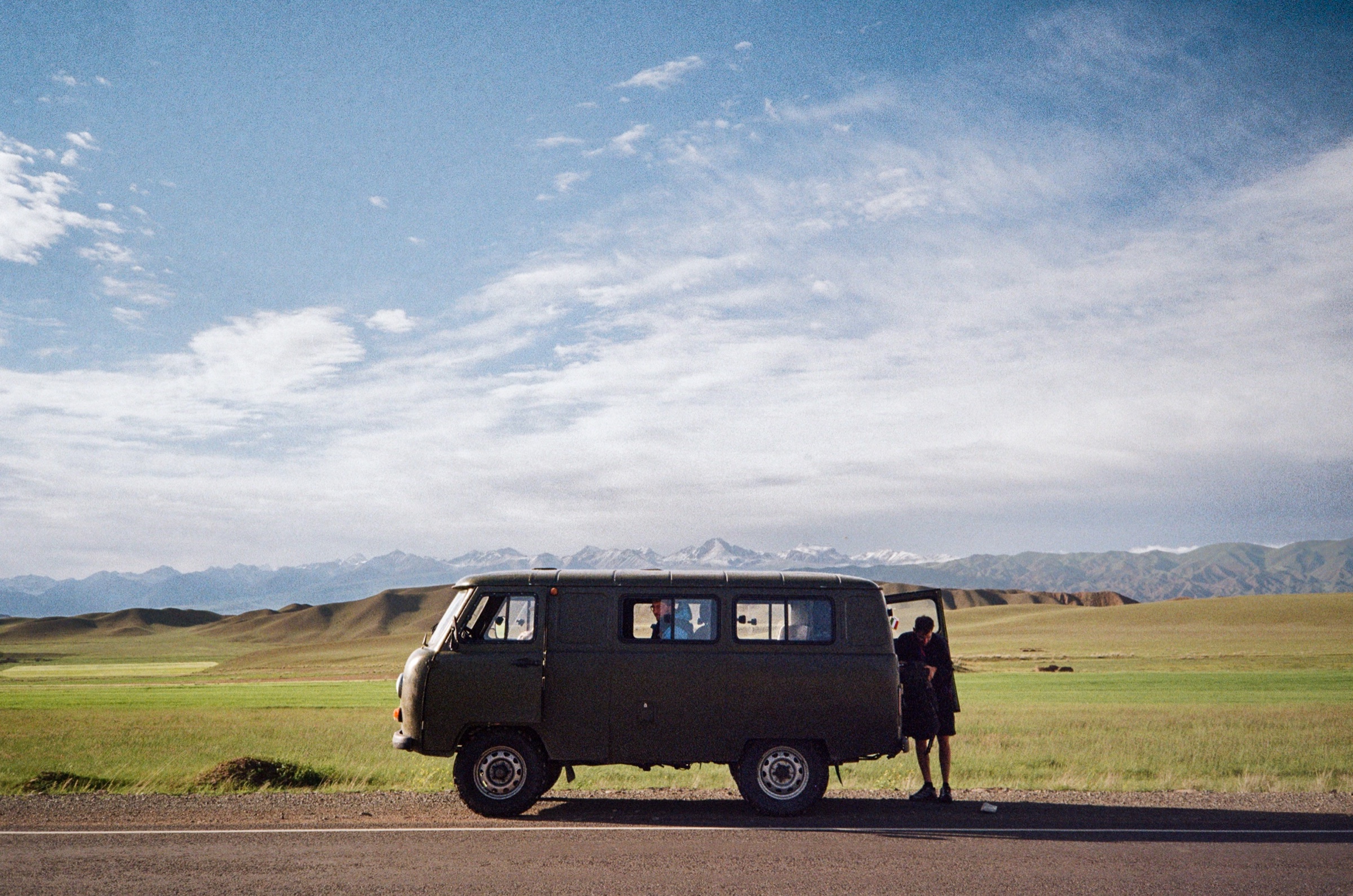 Soviet UAZ van parked on an empty road with snow-capped Tien Shan mountains in the distance, Kyrgyzstan - Travel photography by Rocco Goldschmidt