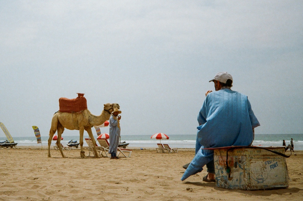 Boy sitting on a wall in a narrow alley with the ocean visible in the distance in Agadir, Morocco - Street photography by Rocco Goldschmidt