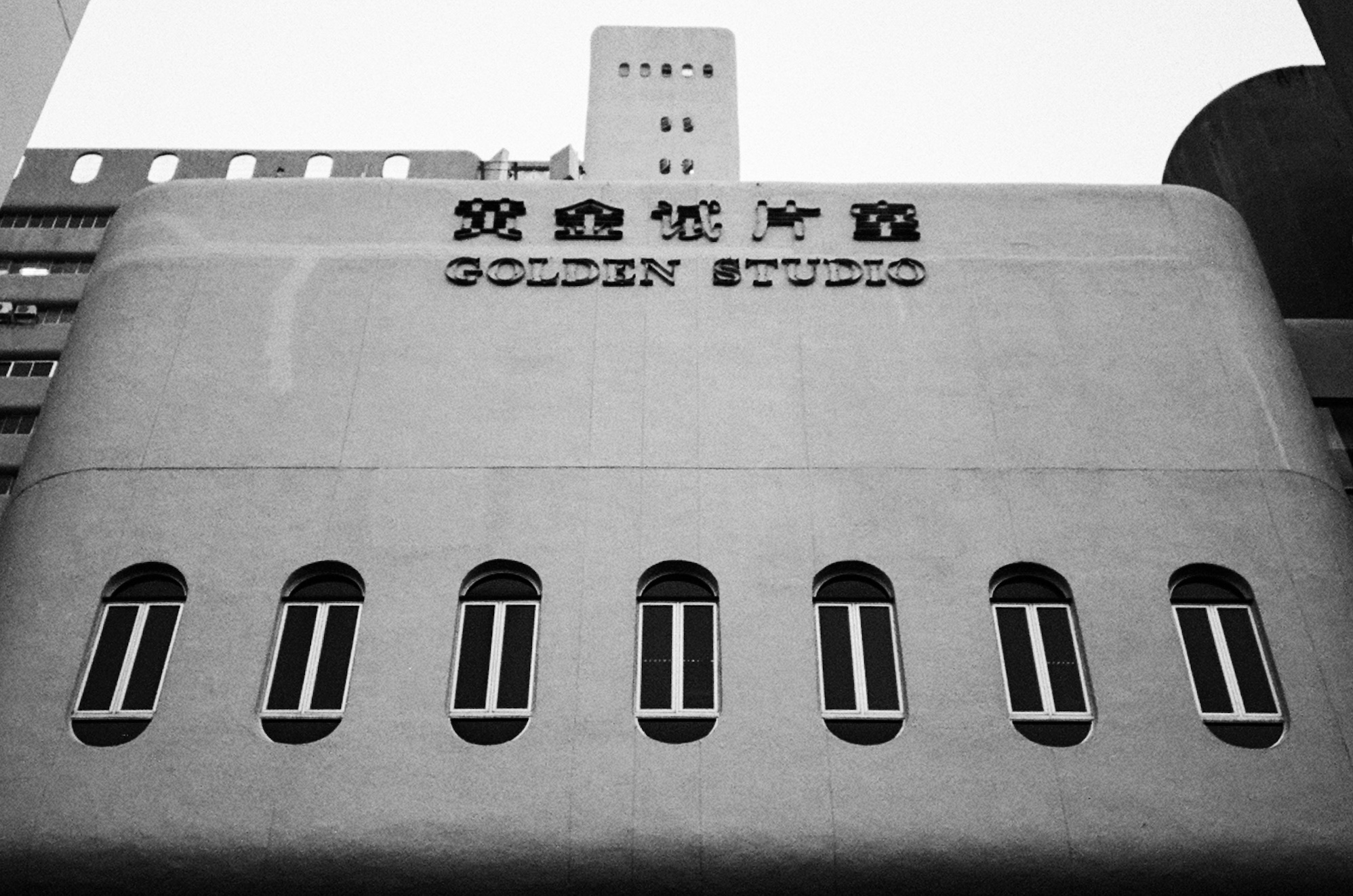 Black and white facade of the Golden Studio building, a rounded concrete wall with a row of arched windows - Film photography by Rocco Goldschmidt