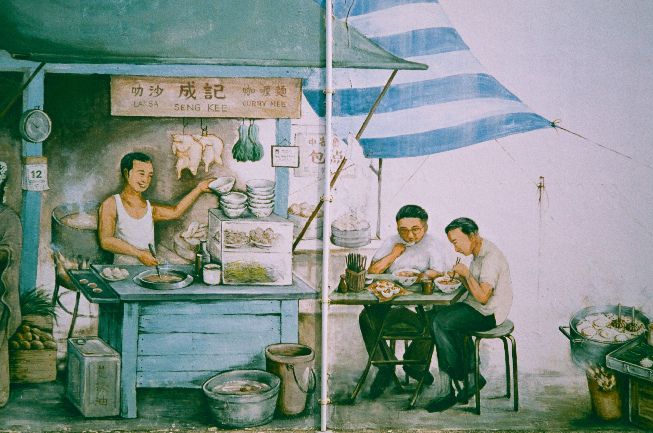 Mural of a laksa and curry mee hawker stall, with a cook serving and two men eating under a striped awning - Film photography by Rocco Goldschmidt