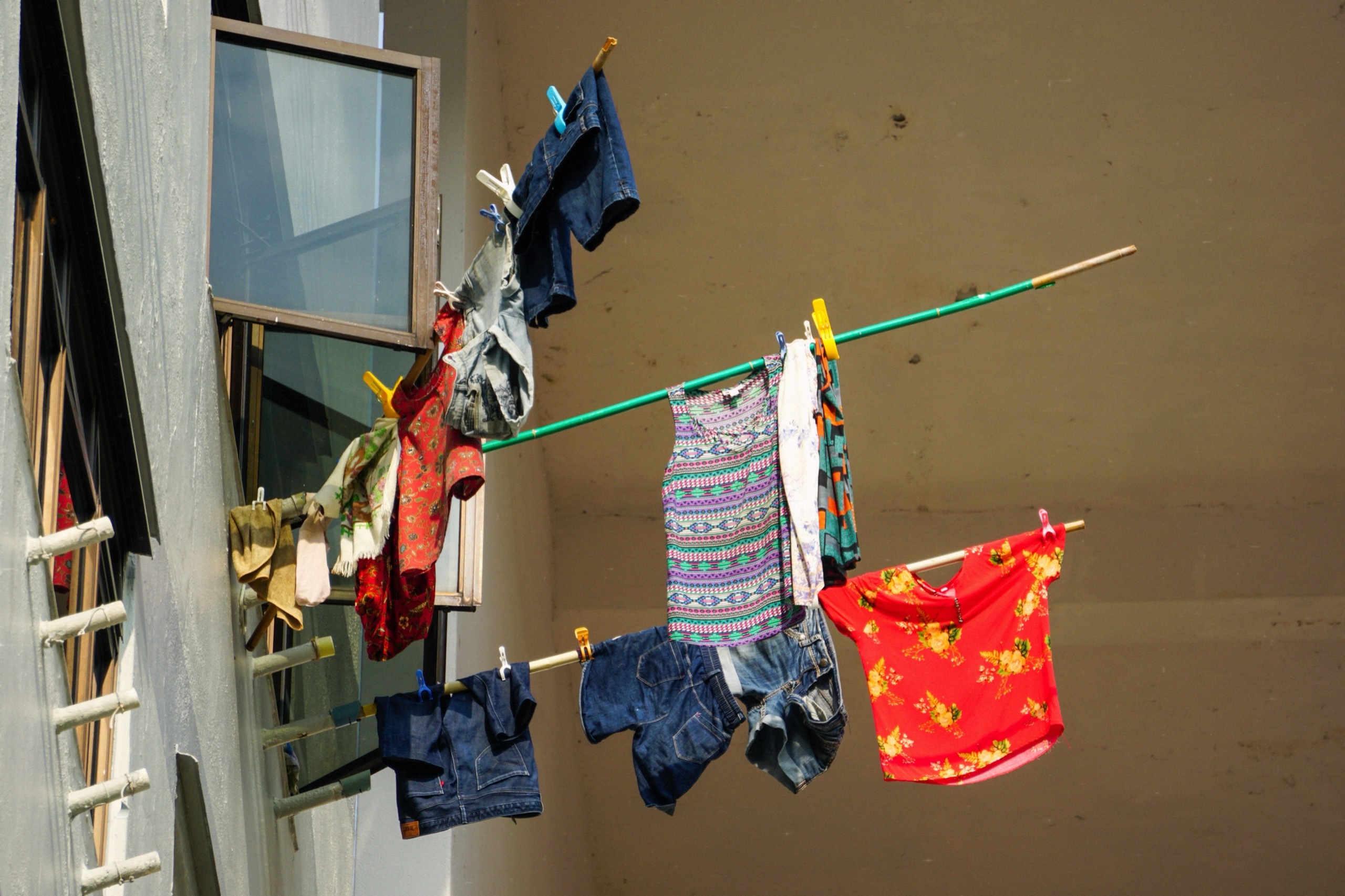 Colourful laundry drying on bamboo poles sticking out of a housing block window in Singapore - Street photography by Rocco Goldschmidt