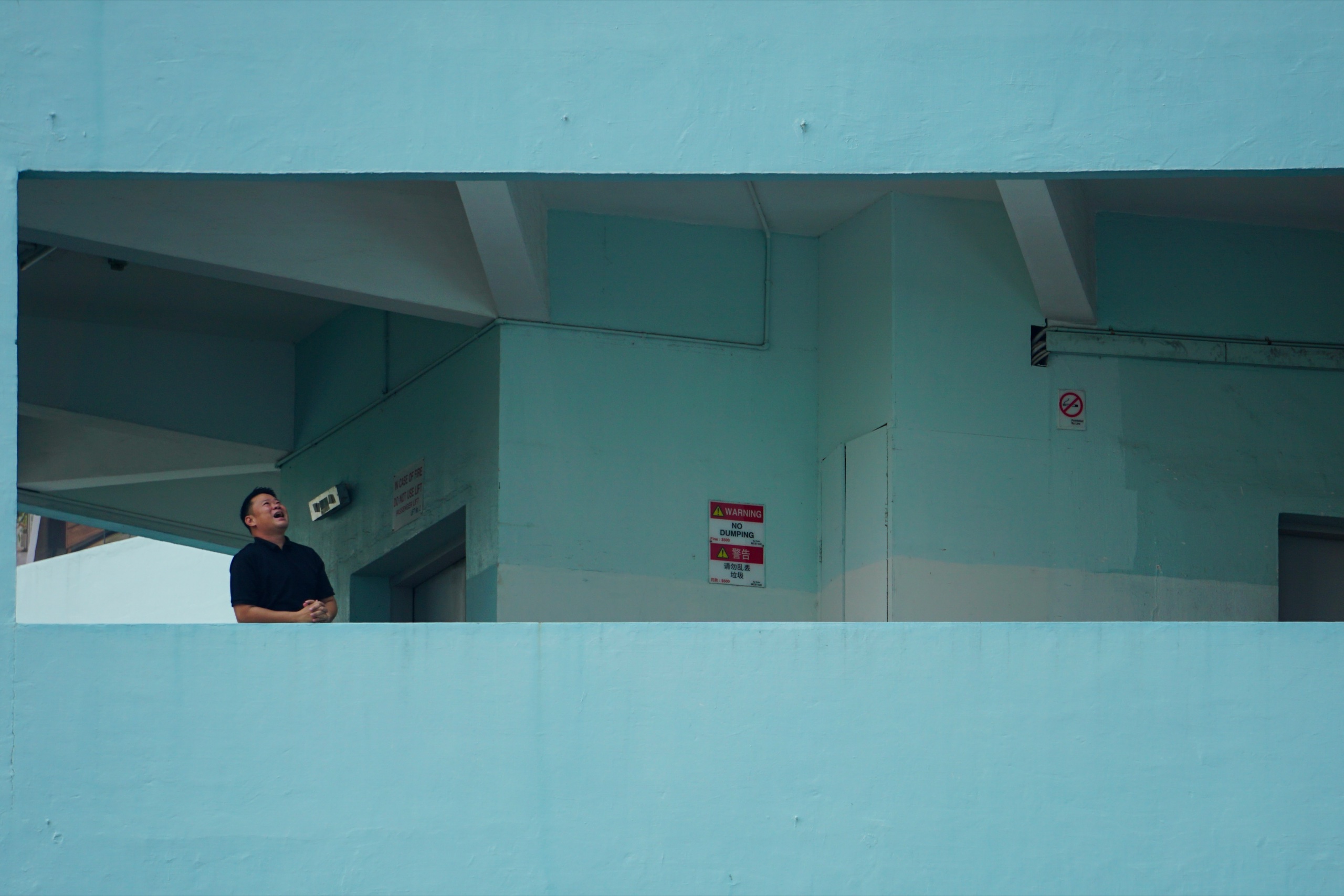A man laughing and looking up, framed by a long rectangular opening in a turquoise concrete wall - Photography by Rocco Goldschmidt