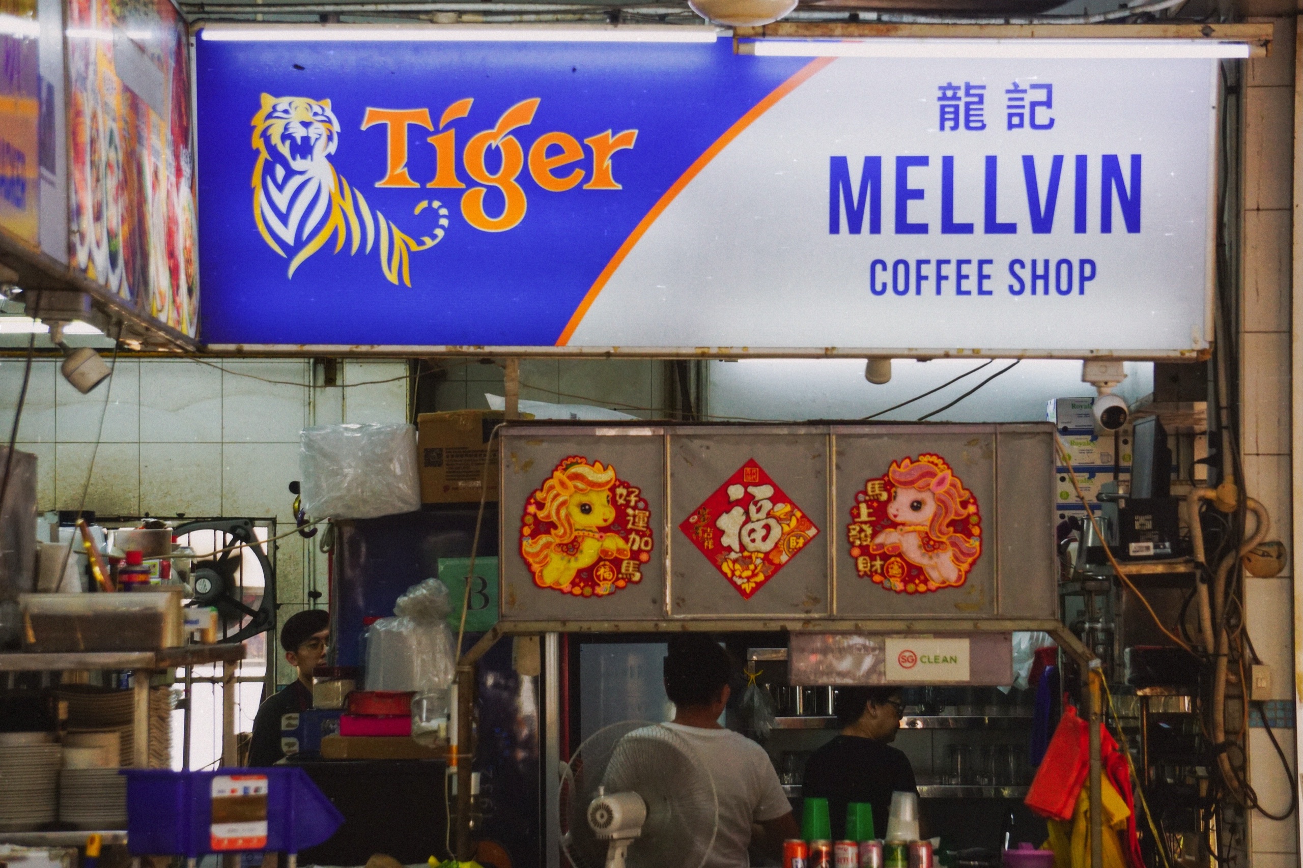 Mellvin Coffee Shop drinks stall under a Tiger beer sign, with lunar new year decorations and staff at work, in Singapore - Street photography by Rocco Goldschmidt