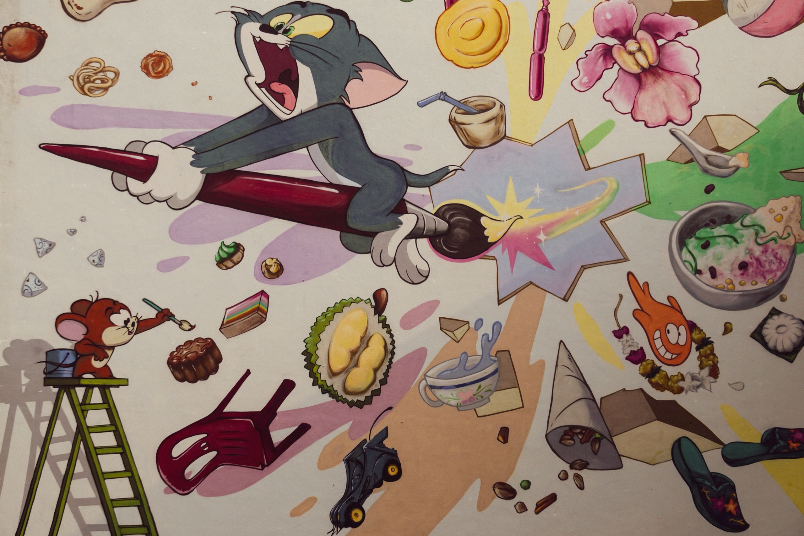 Tom and Jerry mural with Tom riding a paintbrush through flying local snacks and durian in Singapore - Street art photography by Rocco Goldschmidt