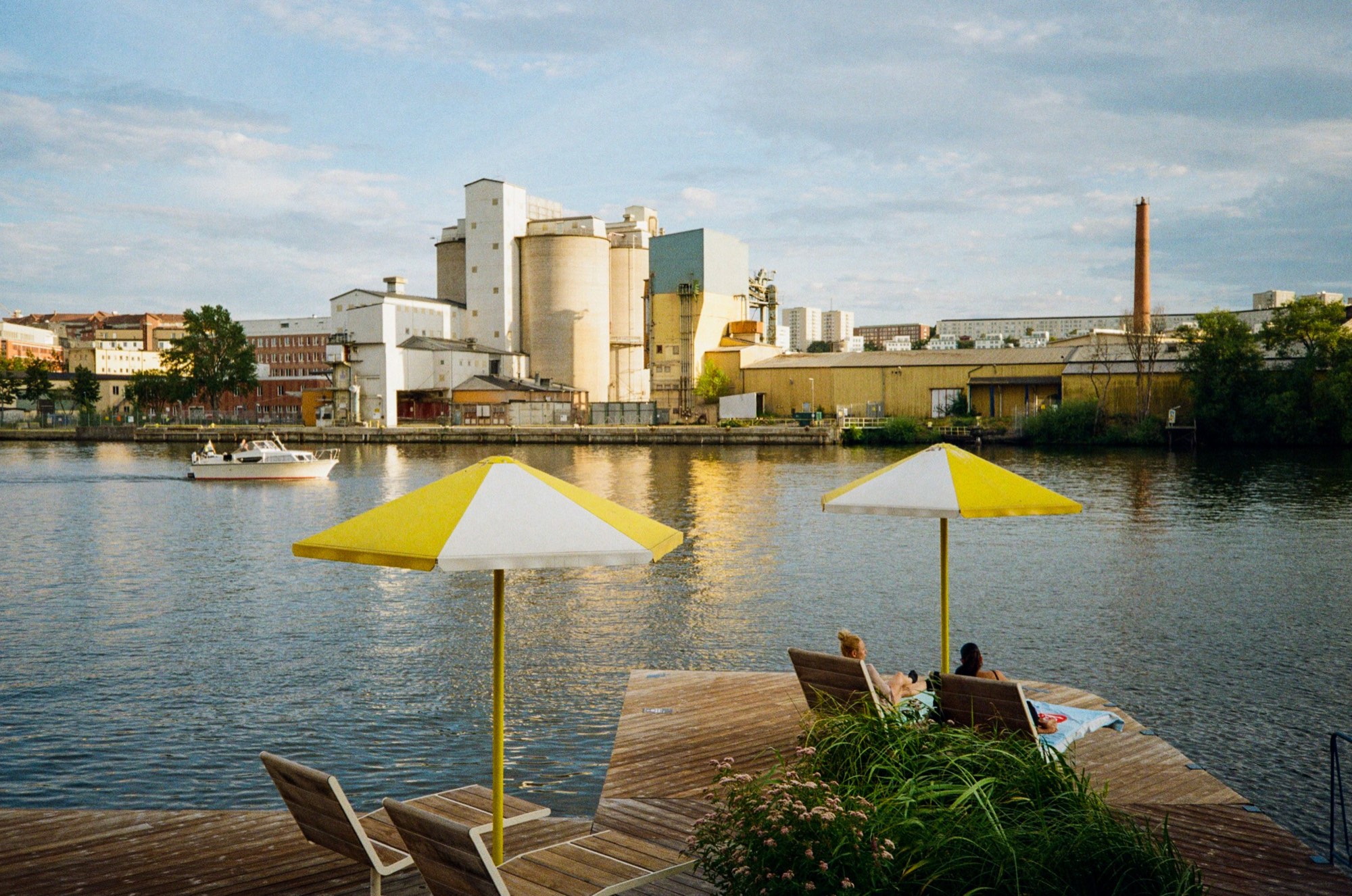 Yellow parasols and deck chairs on a wooden jetty facing an industrial waterfront in Stockholm, Sweden - Summer photography by Rocco Goldschmidt